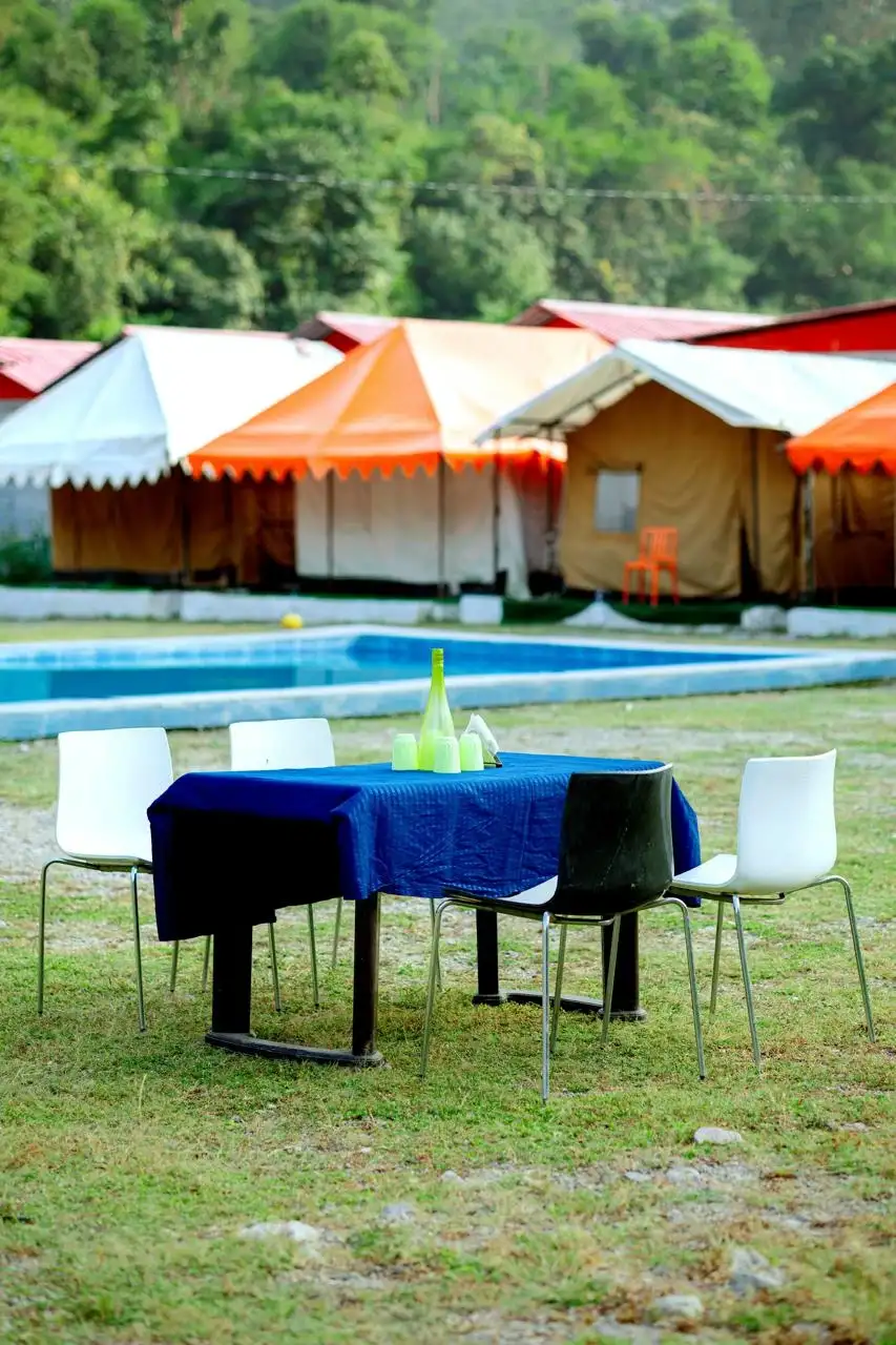 Outdoor dining setup near swimming pool at RS02 camping resort with tents in background